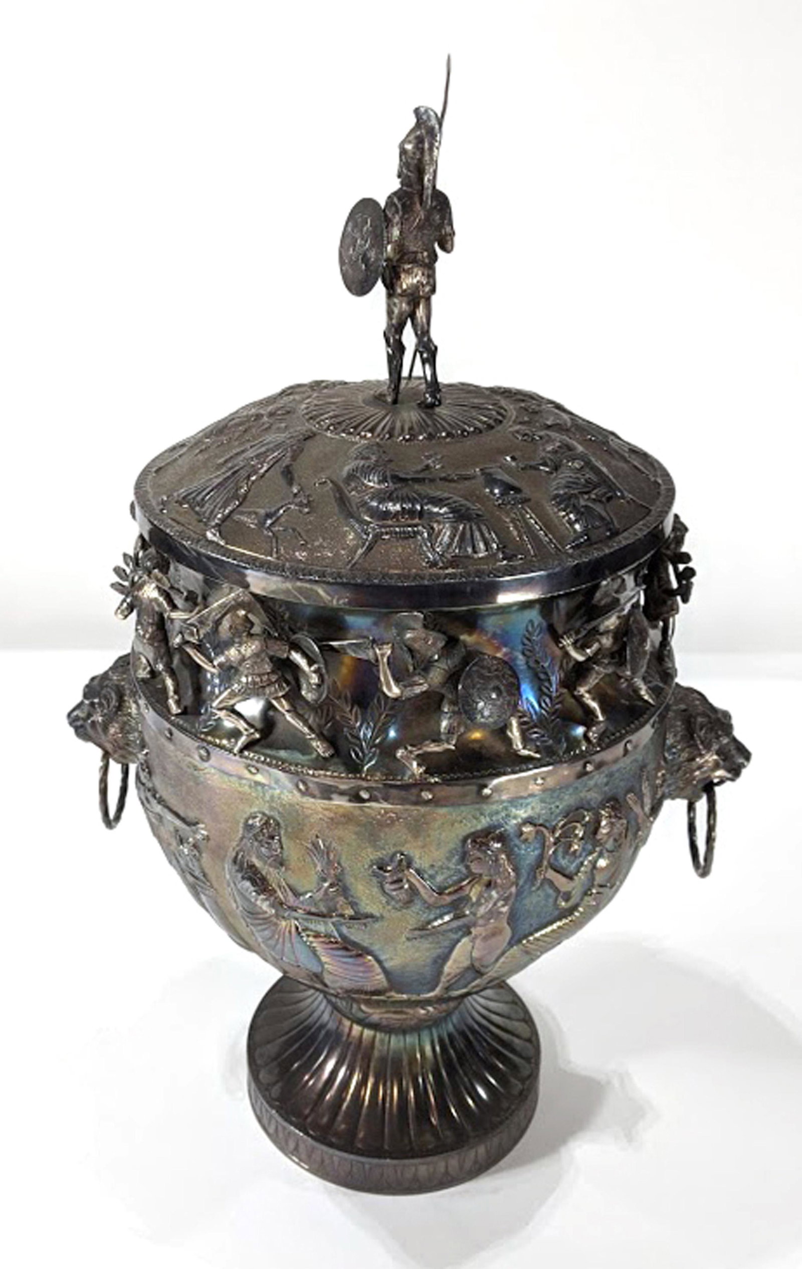 A continental Renaissance Revival silverplate covered: A continental Renaissance Revival silverplate covered urn circa 1860, having a figural finial of a warrior above the chased and relief decorated friezes depicting a battle scene and genre scenes in th
