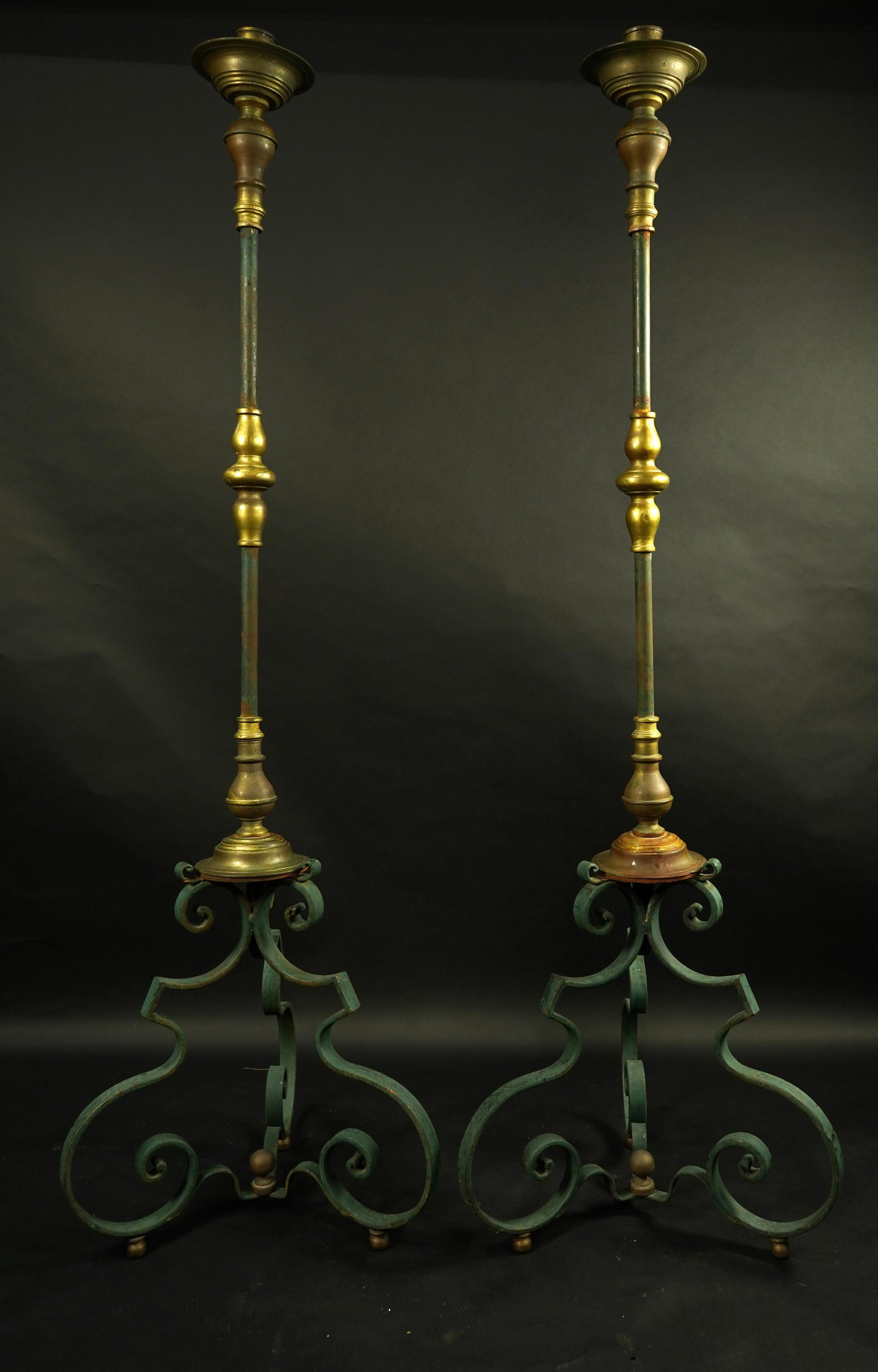 A pair of Baroque style iron and brass torchieres: A pair of Baroque style iron and brass torchieres, each having a turned standard with green patina, and rising on a tripod base, 71"h Property from the Estate of Frank J. Caufield, San Francisco (CA) 