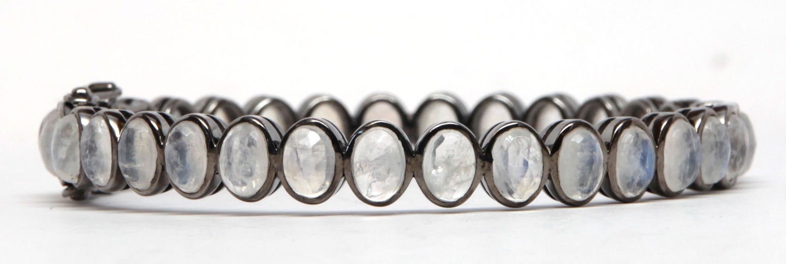 Moonstone, blackened silver bracelet: Moonstone, blackened silver bracelet Featuring (31) faceted, oval moonstone cabochons, measuring approximately 7.0 X 4.5 mm, set in a blackened silver, hinged bangle mounting, measuring approximately