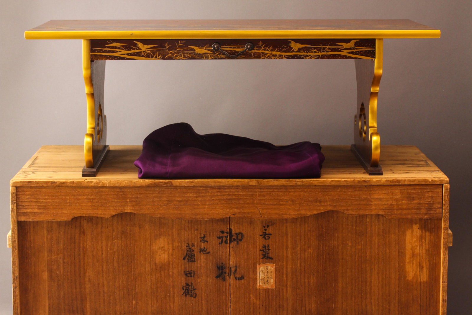 A Japanese Wooden Maki-e Gold Lacquer Book Desk: A Japanese wooden Maki-e gold Lacquer book desk with cranes and reed decoration. Label on the box "ShoukenKoutaigou Goyumotsu, Taishou Sannen Kugatsu Nijiyuugonichi, Gohairyo". Size: 10"h x 14.65"w, w