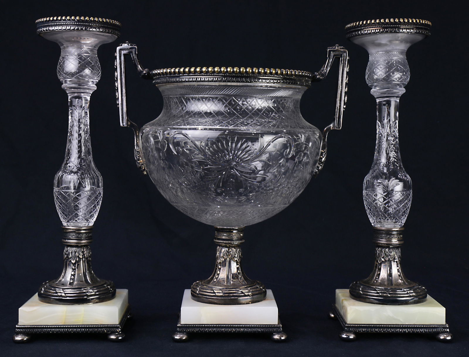 A Pairpoint garniture set: A Pairpoint garniture set, consisting of an urn having a cut glass bowl with Neoclassical style accents, and two candlesticks, each having a baulster form standard, and marked on underside, largest: 1