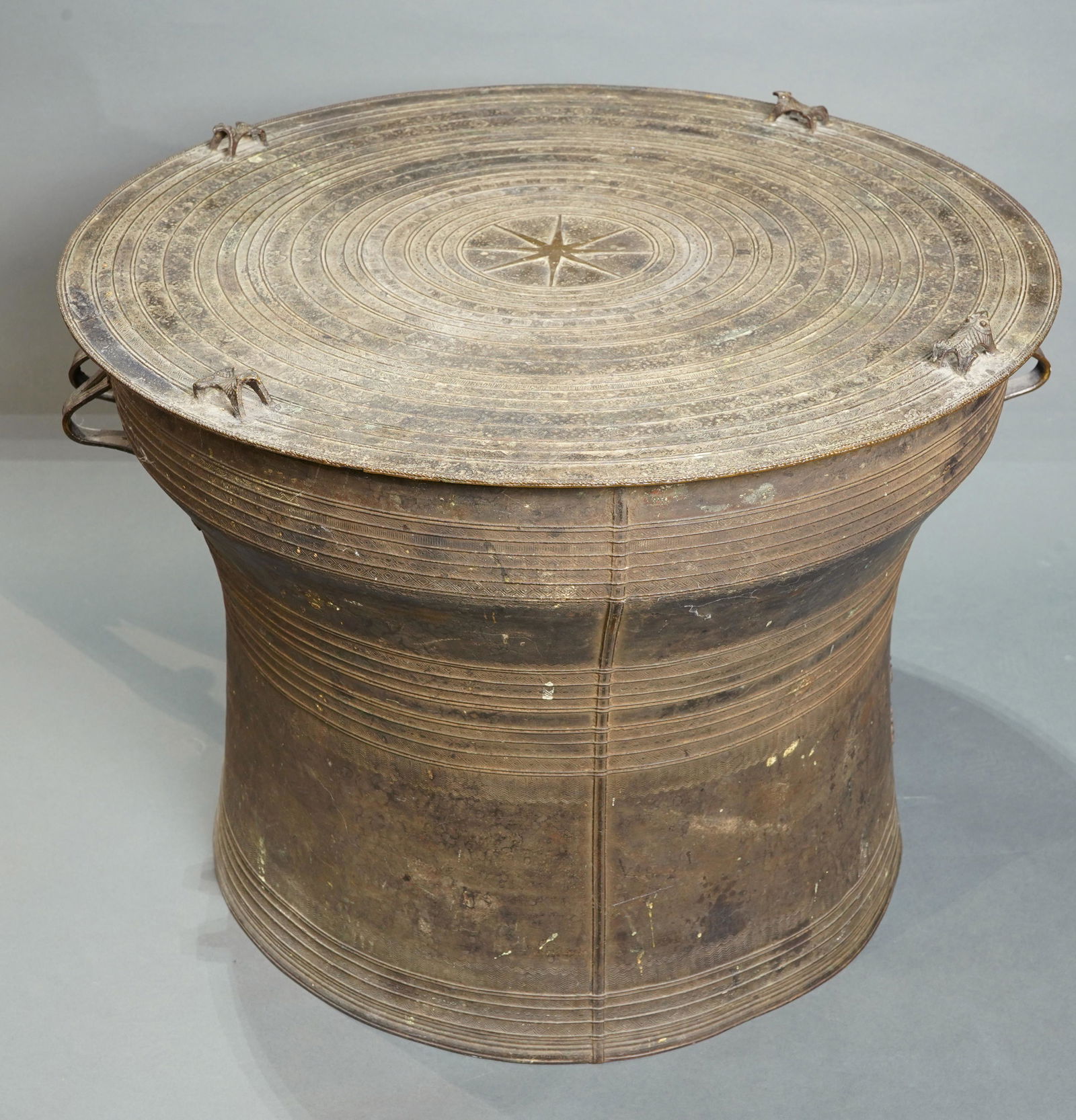 Southeast Asian patinated metal rain drum: Southeast Asian patinated metal rain drum, the separately cast top with a starburst medallion encircled with concentric bands bounding geometric and zoomorphic patterns, the shaped body cast with rais