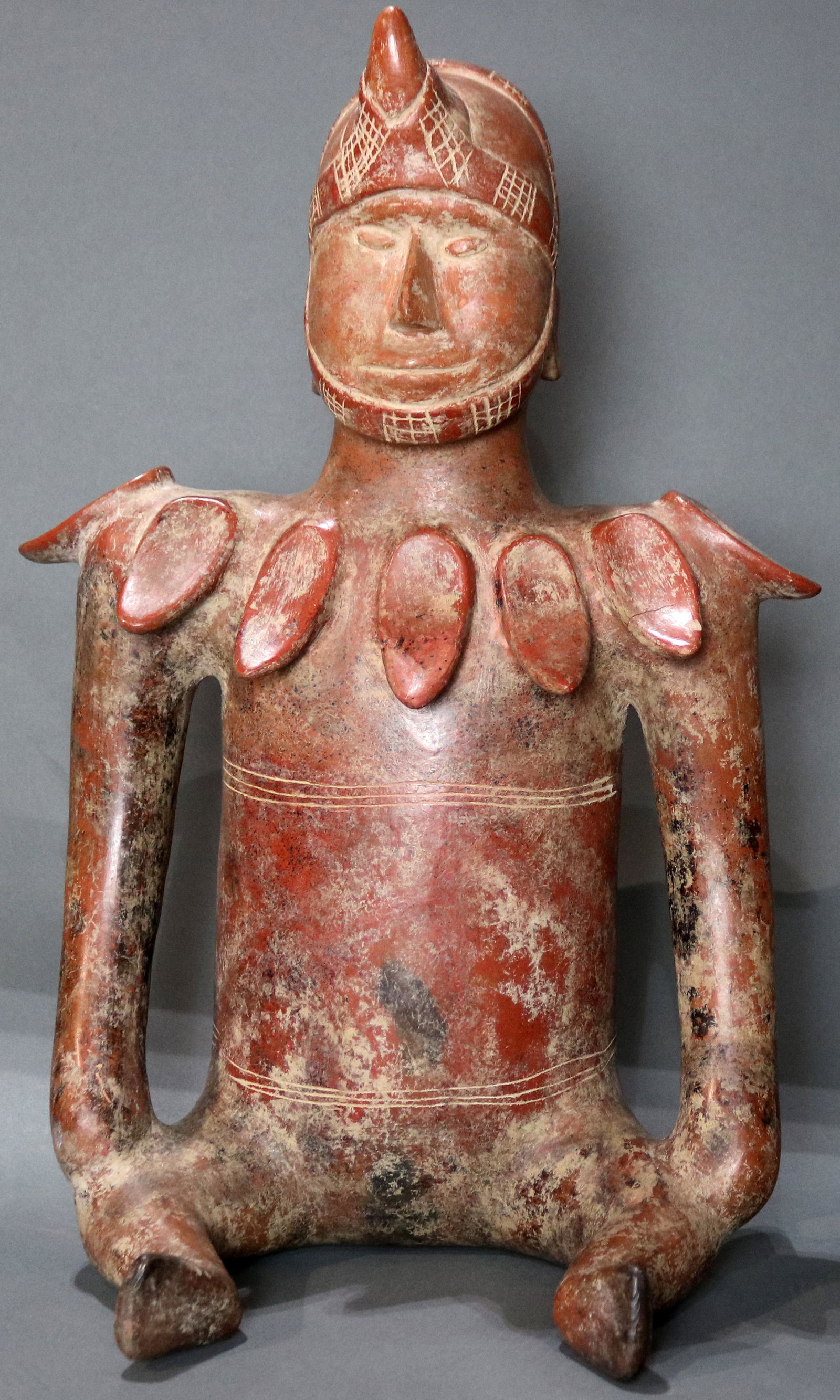 A Pre-Columbian Colima, West Mexico, figure, Ex Ron: A Pre-Columbian Colima, West Mexico, seated shaman, 200BC-300AD, wearing an incised helmet, above a shell decorated neckline, 18.5"h (note: one shell missing) Provenance: Ex prominent Woodside CA esta