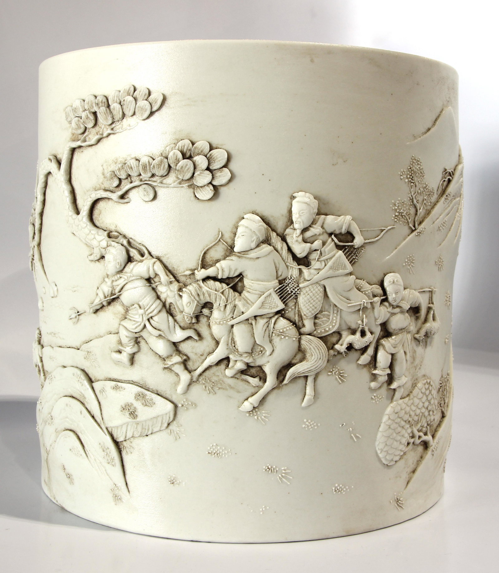 Chinese white glazed porcelain bitong: Chinese white glazed porcelain bitong, the cylindrical form continuously decorated with a hunting scene in a mountainous landscape, Wang Bing Rong mark on base, 6.5"h x 6.75"d
