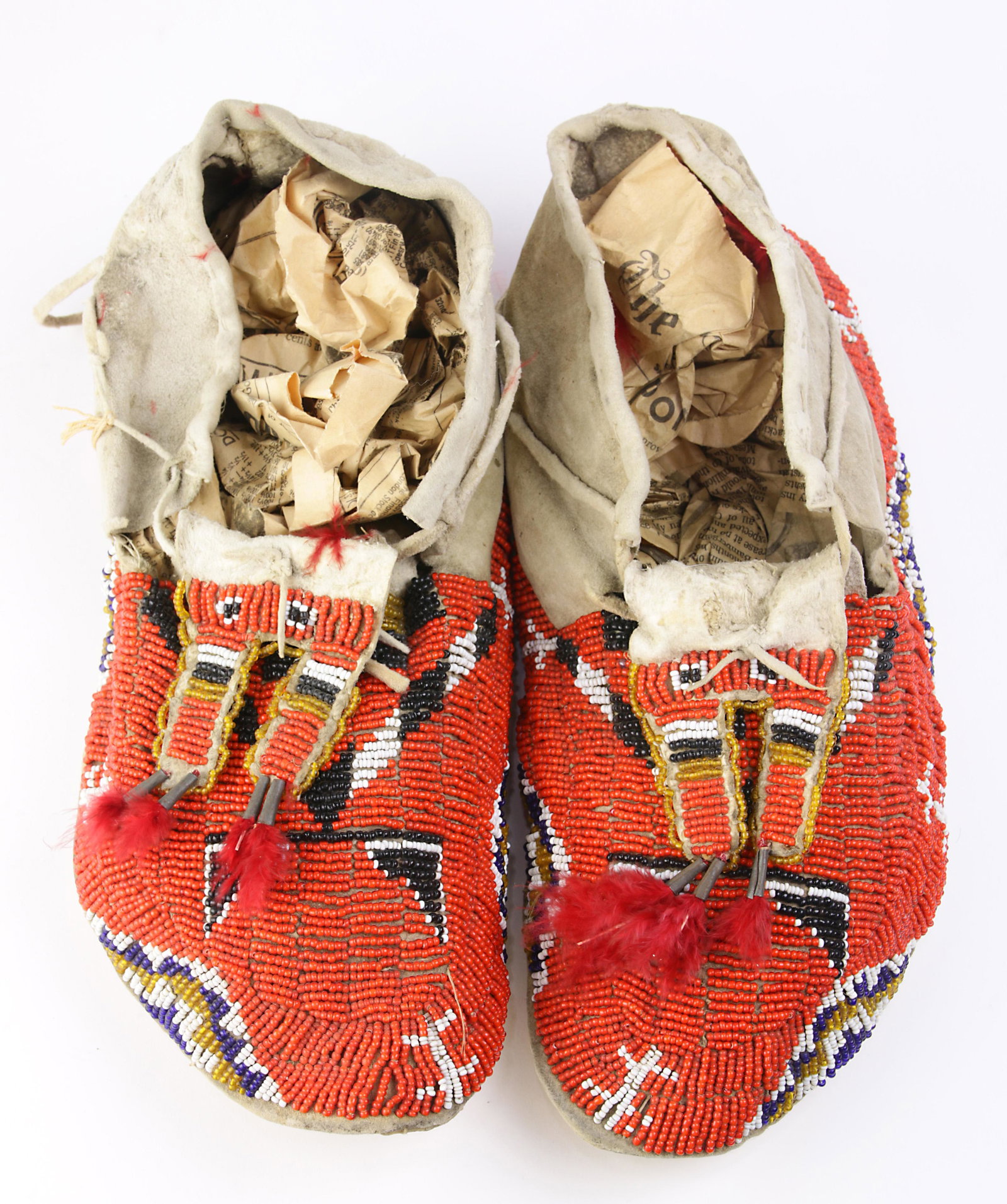 A pair of Plains beaded moccasins: A pair of Plains beaded moccasins, having red beadwork with black and white geometric decoration, 10.5"l