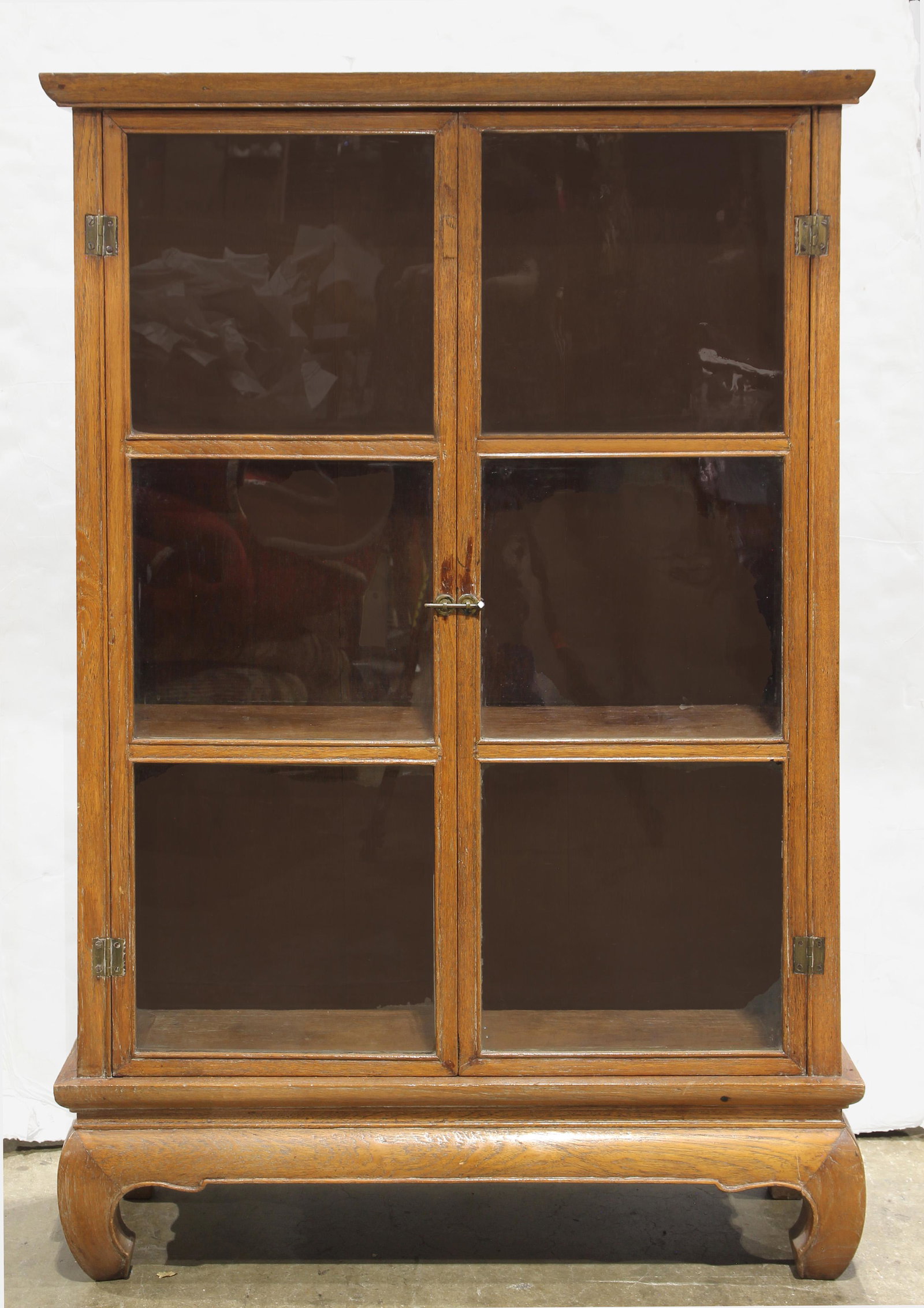 Thai teakwood vitrine: Thai teakwood vitrine, the outset bonnet top over a rectangular case fitted with twin glazed doors, opening to reveal two shelves, rising on cabriole supports, 49.25"h x 32.35"w x 11.5"d. Provenance: 