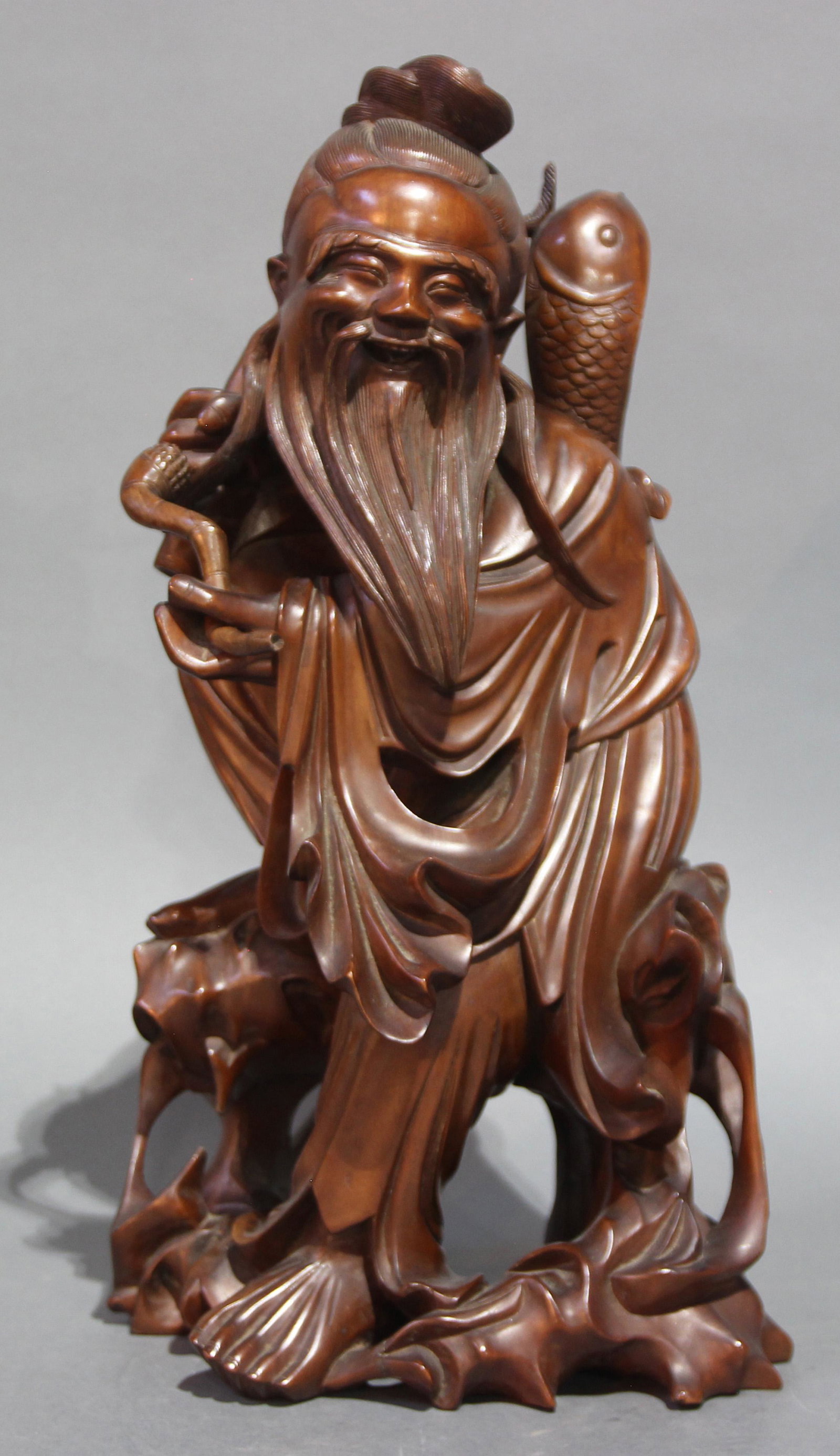 A Chinese Boxwood Figure of a Standing Fisherman: A Chinese boxwood figure of a standing fisher man, shown standing figure wearing long robes and a head wrap, holding a fish on his back, dimensions: 16.5"h x 8"w (41.9cm x 20.32cm).