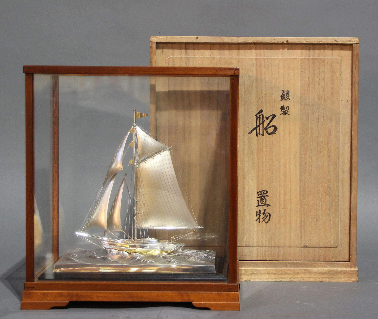 A Japanese Silver Sailboat Model mounted on Wood Base: A silver sailboat model mounted on wood base, comes in glass and wood display case, dimensions with box: 10.75"h x 9.5"w x 6"d (27.3cm x 24.1cm x 15.2cm).