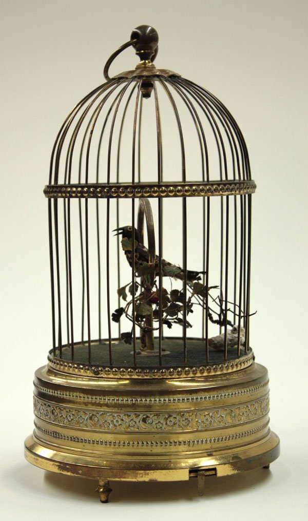 German automaton chirping bird in cage: German automaton chirping black feathered bird in cage, the bird perched on a hoop adorned with a flowering vine, the a forest green velvet cage floor above the patterned cage base, 12''h
