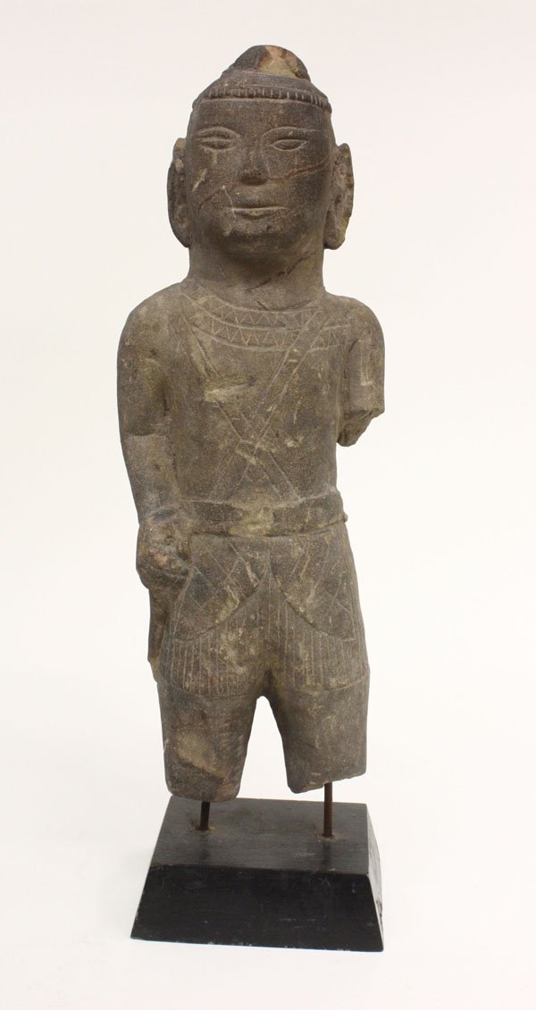 Southeast Asian Stone Figure, Khmer: Southeast Asian stone figure of a divinty, a folk rendering of a Khmer culture male deity standing in a short pleated garment and with one hand grasping a 'sword' (damage), with a black lacquered stan