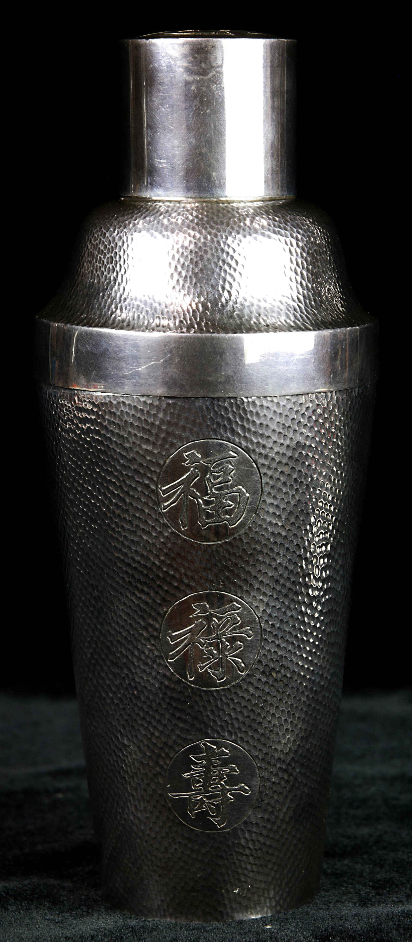 A Chinese Export silver cocktail shaker: A Chinese Export silver cocktail shaker, the tapering cylindrical form, overall decorated with a hammered fish scale design, centering "Fu", "Lu" and "Shou" medallions, Shou medallion on the lid, 9"h,