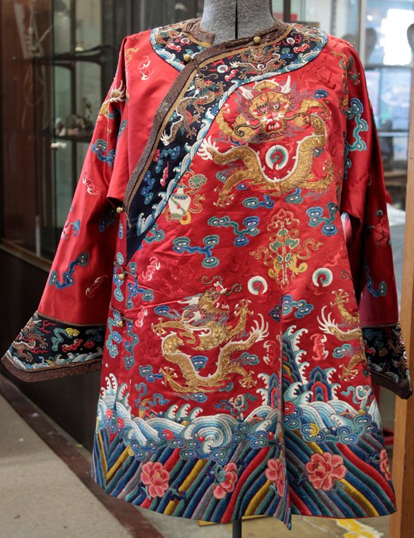 Chinese Child's Dragon Robe: Chinese Manchu-style embroidered red satin ground child's robe, displaying eight dragons couched in metallic threads chasing sacred jewels amid scrolling clouds and auspicious emblems executed with Pe