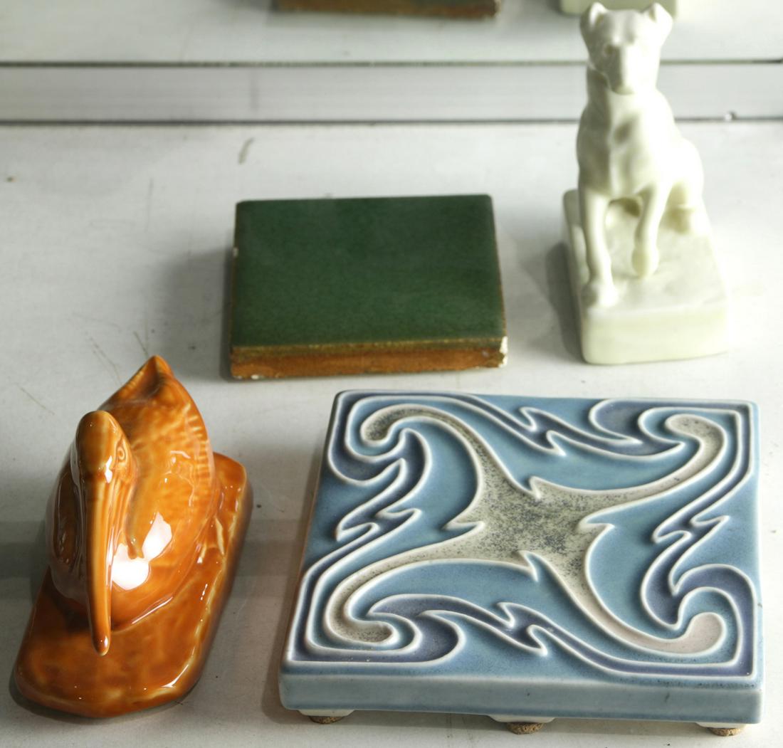 (lot of 4) Rookwood group: (lot of 4) Rookwood group, consisting of a dog paperweight, circa 1931, #2777; a pelican paperweight, circa 1965, #2711; a "Roookwood Faience" green glazed tile (no date), and a blue trivet with geome