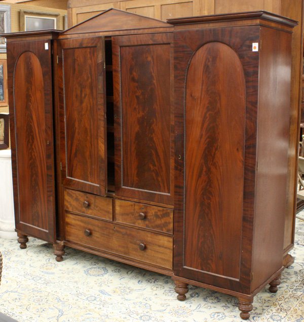 Victorian flame mahogany armoire: Victorian flame mahogany armoire having peaked cornice, beaded moulding, double door center revealing fitted sliding shelves over two short and one long drawer, flanked with cabinets, the whole rising