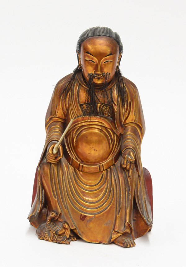 Chinese gilt, lacquered wood figure, male deity: Chinese gilt and lacquered wood figure of a male deity seated in flowing robes accompanied by a pair of snakes by his foot and fitted with a bone sword to his right hand, the sincere face hightened by
