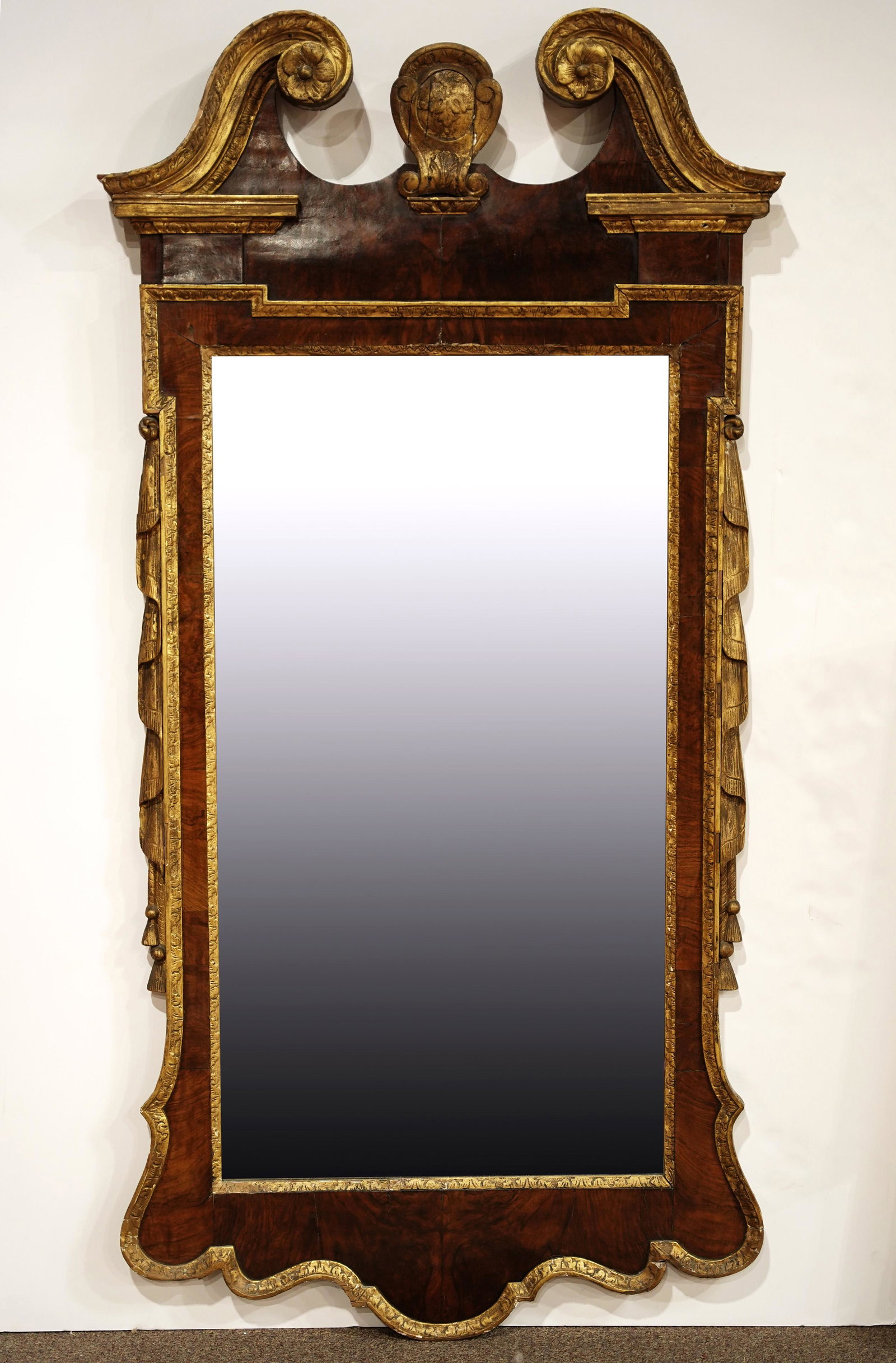 A continental partial gilt and mahogany looking glass: A continental partial gilt and mahogany looking glass circa 1840, having a rosette decorated broken pediment surmounting the original plate glass, 65"h x 32"w