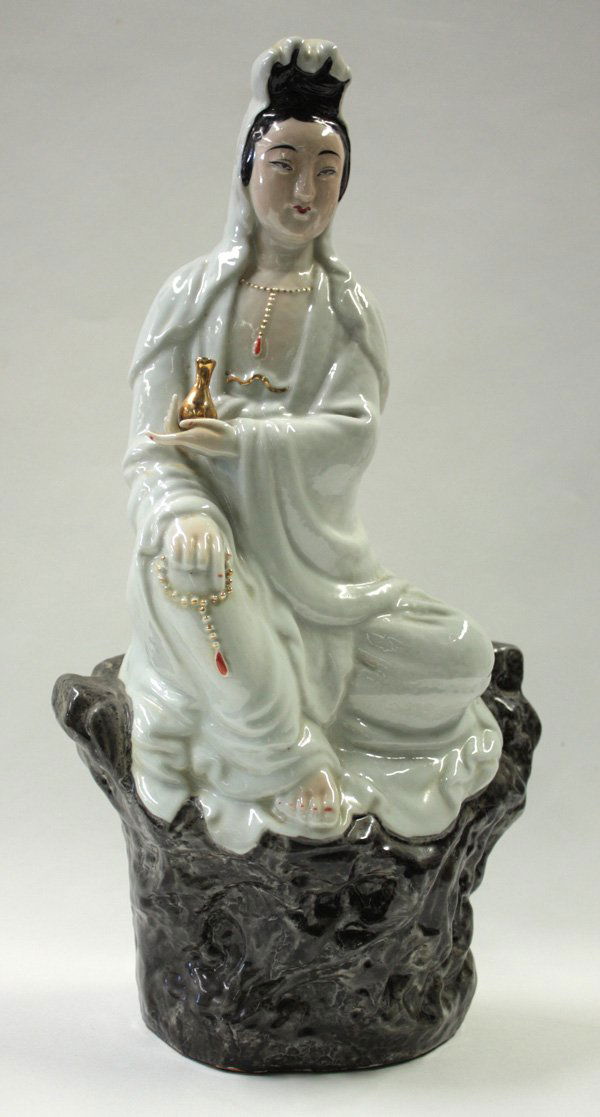 Chinese Seated Porcelain Guanyin: Chinese porcelain figure of Guanyin, seated on rockwork the bodhisattva dressed in loose white robes holds an amphora and with a set of prayer beads resting on her knees, with a white cowl over her ha