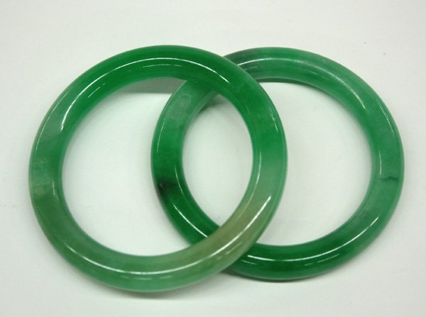 Pair of Chinese Green Jade Bangle Bracelets: Pair of Chinese hardstone bangle bracelets, each of ring form and fashioned from a mottled green matrix flecked with light and dark inclusions. 3''outer diam; 2.25''inner diam