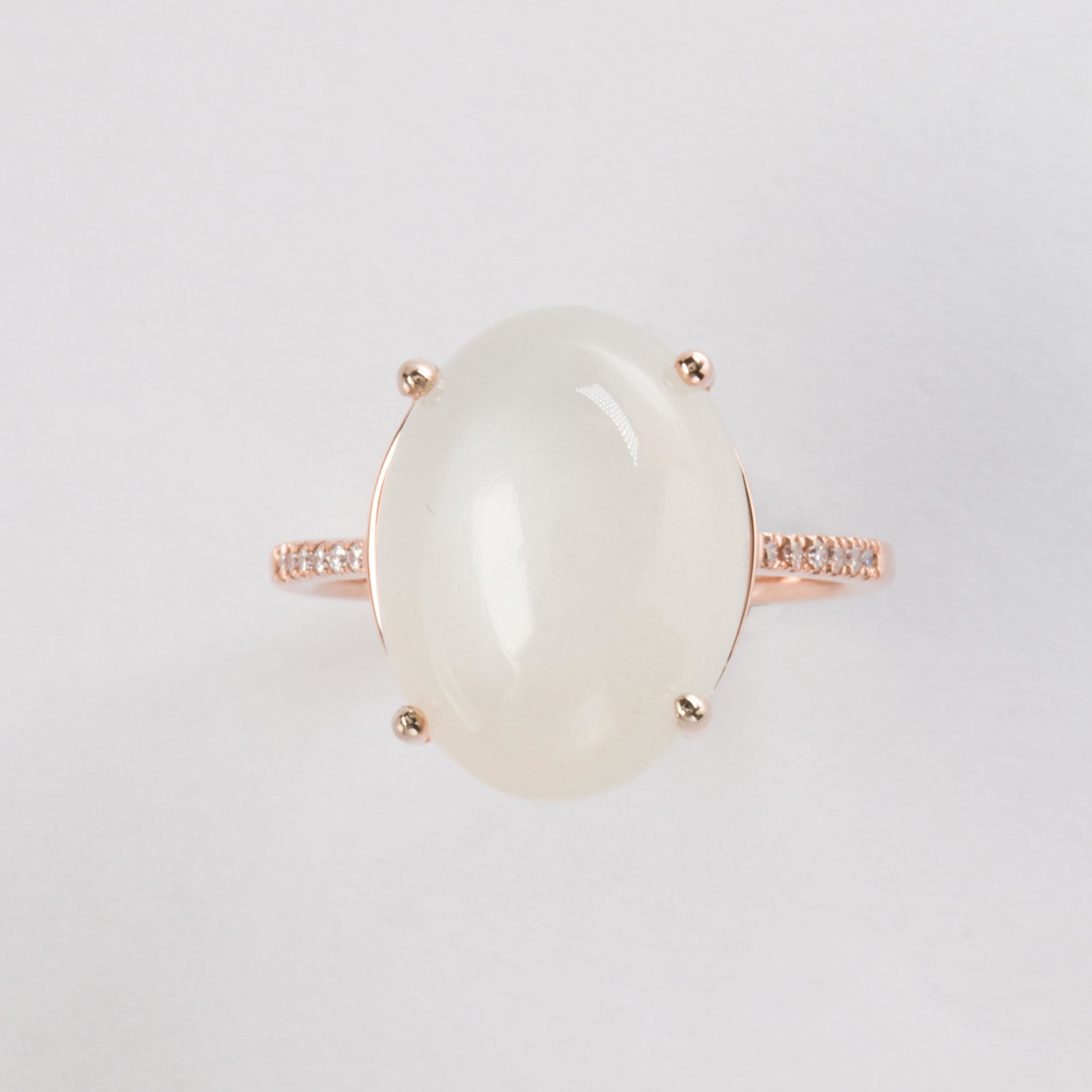 A moonstone and fourteen karat rose gold ring: A moonstone and fourteen karat rose gold ring designed as an oval cabochon moonstone, measuring approximately 16.0 x 12.0 x 7.1 mm, flanked by round brilliant-cut diamond shoulders. 3.0 dwt; Size: 7 1