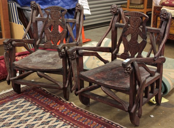 Pair African Ebonized Wood Armchairs: Pair of African ebonized armchairs, each with the openwork back splat carved with a central figural plaque flanked by stylized figures at either end and supporting the side arms, 34.5''h