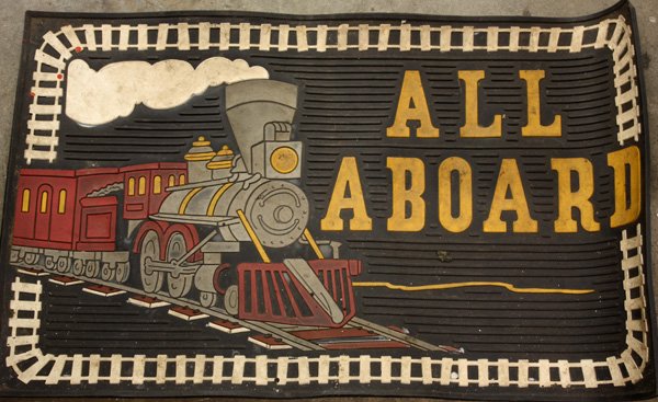 Model train tracks, magazine: One shelf of model train related items including O gauge track, a rubber footmat ''All Aboard'' depicting a steam locomotive, copies of 1960's Model Railroader magazine