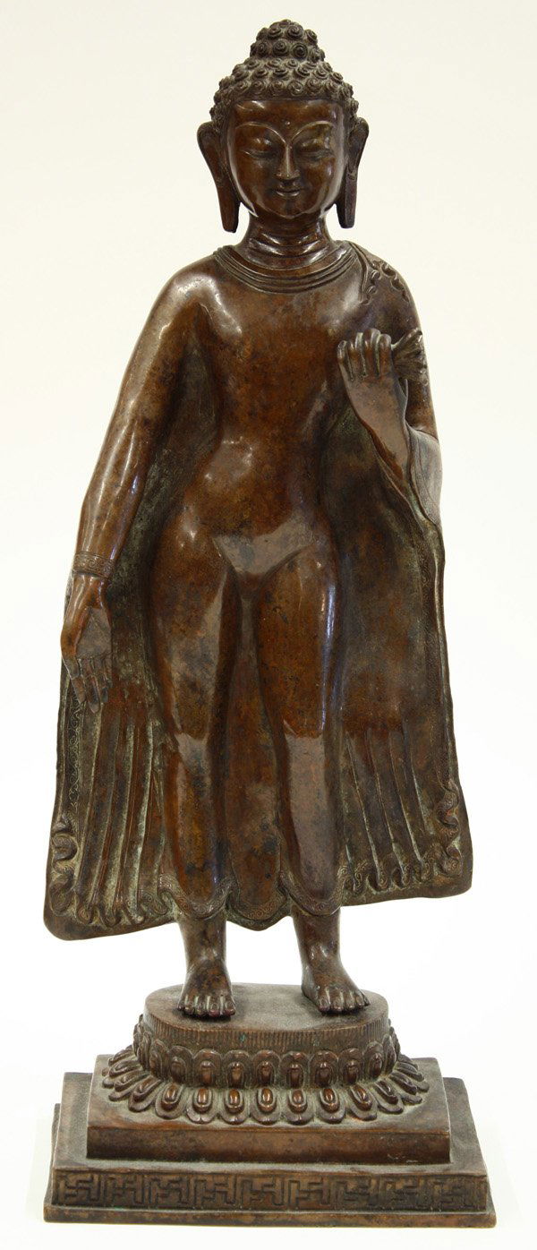 Himalyan Copper-Alloy Buddha Figure: Himalyan patinated copper-alloy figure of the Buddha, standing in a diaphonous robe revealing his abhanga stance, his left hand clutching the brocade patterned hem, the other displaying the varada (ge