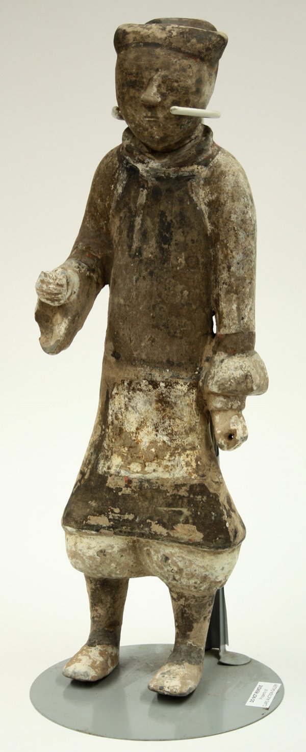 Chinese Han Painted Pottery Funerary Figure: Chinese painted grey pottery figure of an attendant, Han Dynasty (206 BCE-220 CE), standing in attention with his right arm extended, the somber face with the soft cap of an official and wearing a hea