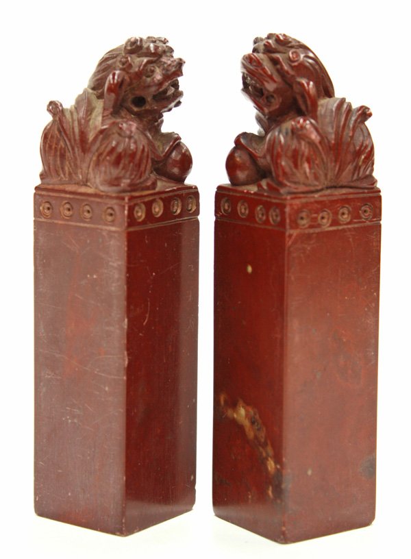 Chinese Soapstone Seal, Fu-lion: Pair of Chinese soapstone seals, each with a tall rectangular shaft supporting a seated fu-lion with one paw resting on a ball, the deep red matrix mottled by russet inclusions, base uncarved, 4.1''h