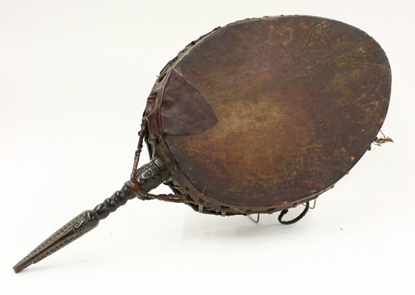 Tibetan Buddhist ritual drum: Ceremonial Tibeten Buddhist ritual drum with rattan binding and carved wooden handle decorated with stylized masks, 19''d; Note: patch on one side of drum