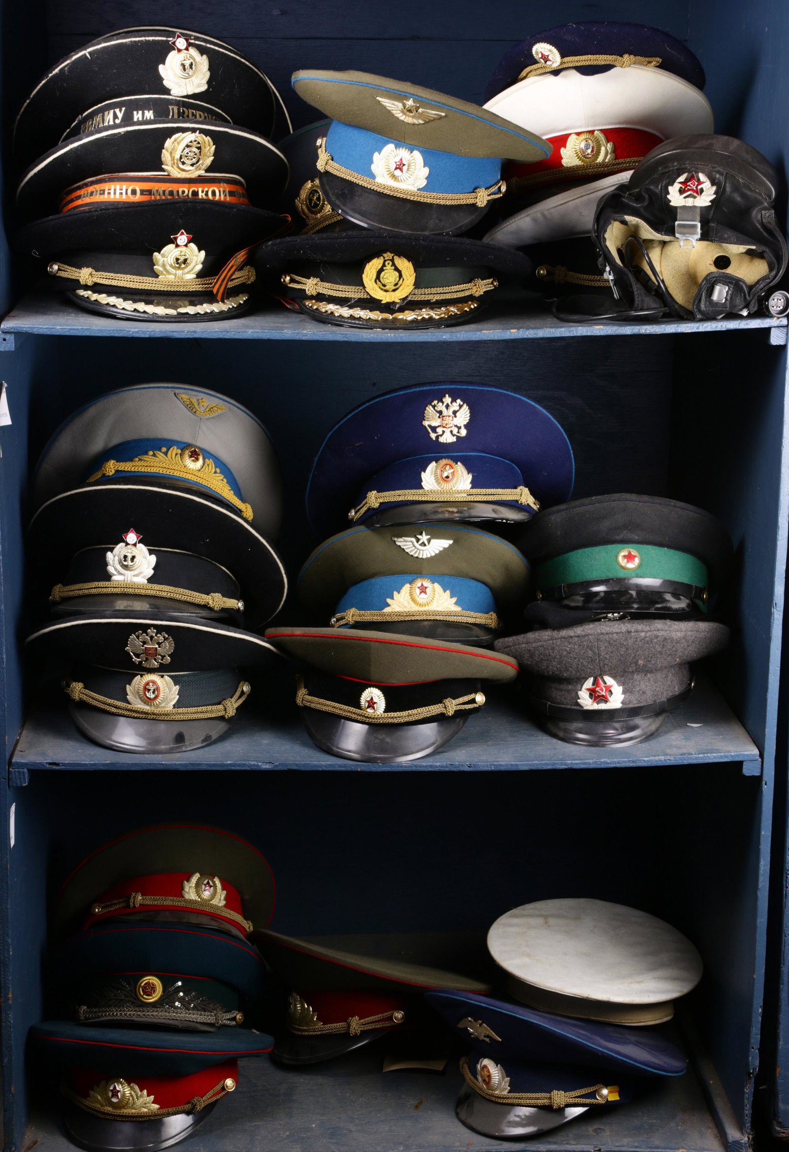 Three shelves of mostly USSR air force hats: Three shelves of mostly USSR air force hats: including a USSR Air Force Chief Marshall full dress hat, USSR prison guard hat, USSR motorized rifle hat; others include a Russian Army officer, etc. Prov