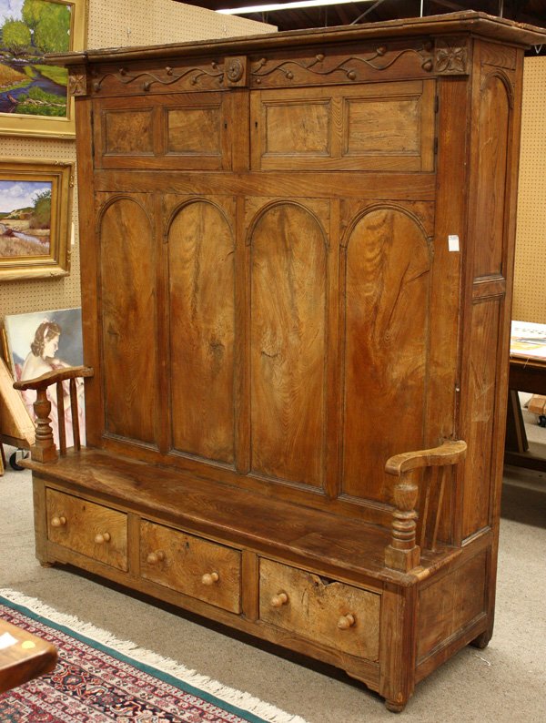 Irish carved chestnut box settle: Monumental Irish carved chestnut box settle, late 18th century having molded cornice, relief carved frieze with acorns, double door top above arch panels, shaped arms over triple drawers, the outside 
