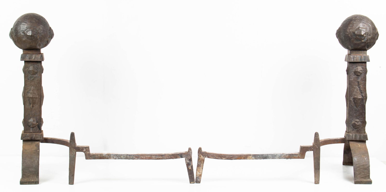 A pair of Spanish Revival style andirons: A pair of Spanish Revival style andirons, each having a hammered spherical finial, above a geometric decorated standard, 24.5"h