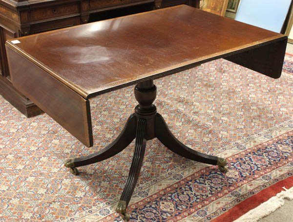 Regency style drop leaf mahogany dining table: Regency style drop leaf mahogany dining table, the top having a fruitwood band inlaid border, above a base having a turned standard supporting four reeded legs, ending in brass capped casters