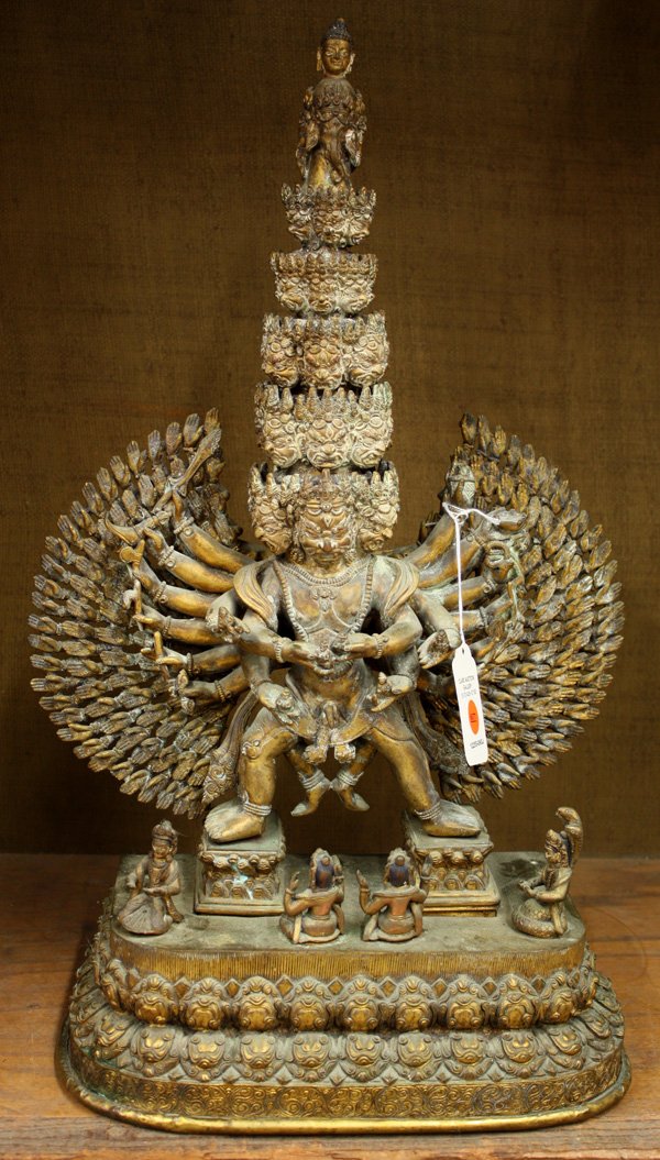 Nepalese Gilt Copper-Alloy Dharmapala Figure: Nepalese gilt copper-alloy figure of a multi-headed dharmapala, 19th/20th century, with seven tiers of heads, most with a fierce expression, the partially nude figure with eighteen primary hands holdi
