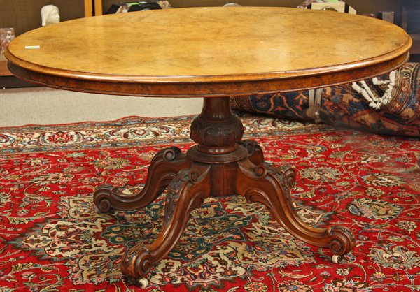 Oval tilt top breakfast table: Oval tilt top breakfast table having a turned support with acanthus leaf carving, rising on a quadrupel pedestal base with relief floral accents and terminating in scroll carved feet with bellflower d