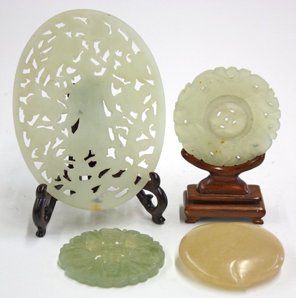 Group Chinese Jade Carvings: (lot of 4) Chinese jade decorations: one peach form belt hook of tan color mottled by light flecks; a circular plaque centered by a movable disk; a medallion pierced with shou character, bats and cash