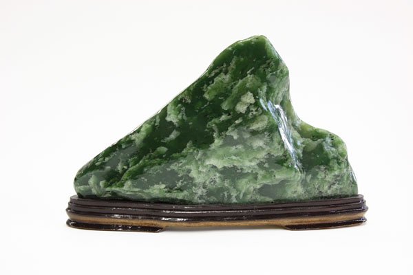 Jade Scholar's Rock: Chinese jade scholar's rock, shaped as a mountain peak, the dark green matrix mottled by patches of lighter inclusions, with wooden stand, overall: 12.25''l