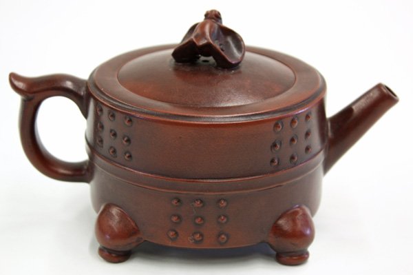 Yixing Ware Chinese Teapot: Chinese Yixing ware tea pot, the short cylindrical body heightened by raised bosses all above four hoof supports simulating a metal vessel and set with an spout opposed by a shaped handle, the lid sur