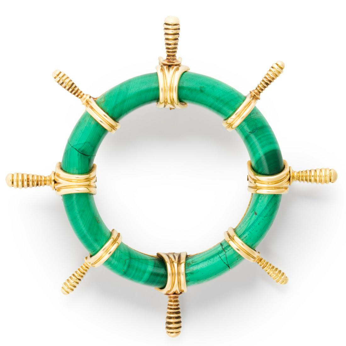 A French malachite and eighteen karat gold brooch: A French malachite and eighteen karat gold broochdesigned as a ship's wheel, with carved malachite fellow and gold handles. 30.1 dwt; length: 3 in