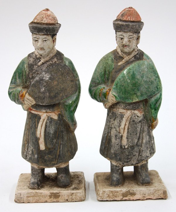 Chinese Glazed Figurines, Ming Dynasty: (lot of 2) Chinese lead glazed figurines, Ming dynasty, each a male attendant figure standing in thick robes and holding a large fan to the front, the face with painted features framed by a tasseled h