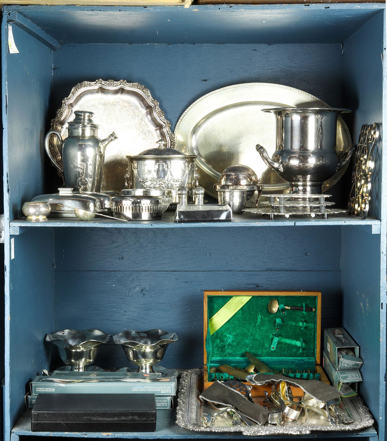 Two shelves as of silver plate table articles: Two shelves as of silver plate table articles, including silver plates serving spoons, ladles, spreaders, a pair of tongs, cased berry spoons, an ice bucket, trivets, an oval tray, a round platter,(2)