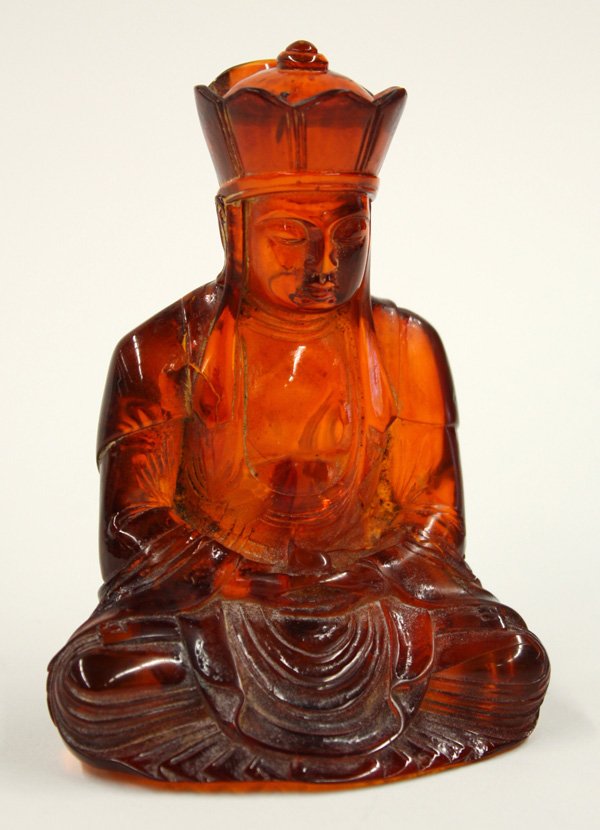 Chinese Amber Buddhist Figural Carving: Chinese amber figural carving, featuring a Buddha seated in meditation with a sacred jewel held to the front, the figure clothed in monastic robes and with a tall five-point diadem framing the serene 