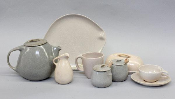 Roseville Raymor stoneware tableware: (lot of 92) Four shelves showing Roseville Raymor modern stoneware tablewares in ivory and grey including water pitchers, teapots, bean pot, celery & olive dish, coffee tumblers, dinner and bread plat