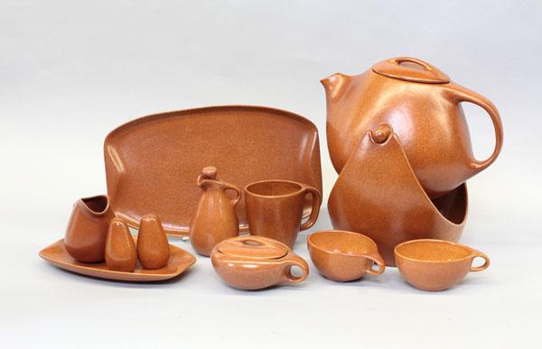 Roseville Raymor tableware: (lot of 98) Three shelves showing Roseville Raymor modern stoneware tableware in terra cotta including dinner, salad, and bread plates, large coffee pot on stand, divided vegetables, salad bowls, lug