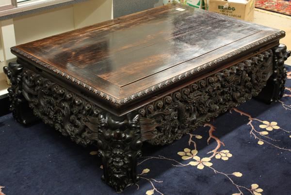 Chinese Ebonized Wood Table: Chinese ebonized wood table, set with a rectangular floating panel within a conjoined petal edge, the wide apron elaborately carved and pierced with pairs of writhing dragons contesting sacred jewels 