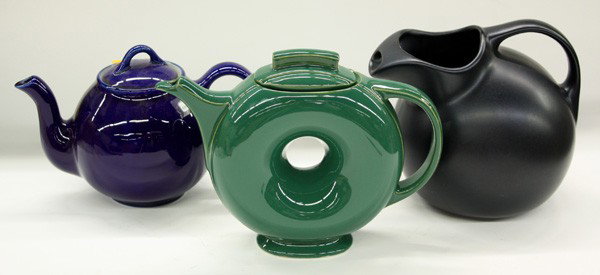 Hall pottery pitchers and teapots: (lot of 8) One shelf displaying Hall pottery pitchers and teapots in various styles and colors including a high glaze grey ''donut'' pitcher