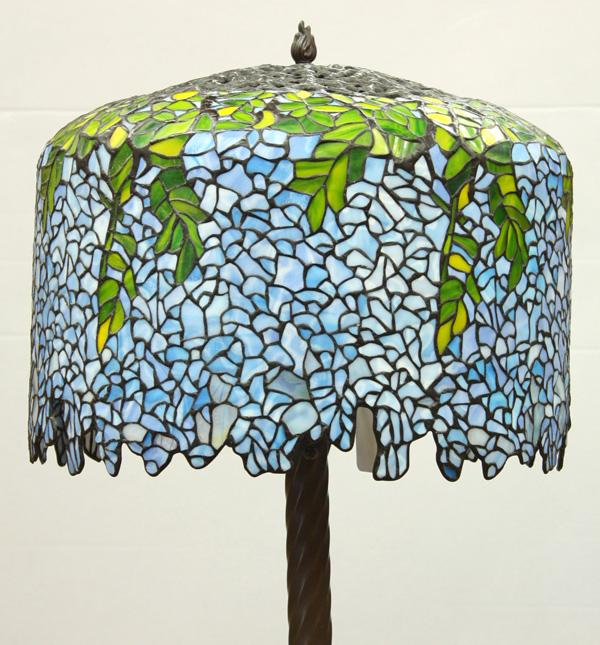 Tiffany Style Leaded Glass Floor Lamp: Tiffany style leaded glass floor lamp, executed in the Wisteria pattern, having a metal openwork top above the green to blue glass, rising on a patinated metal circular base, 65''h