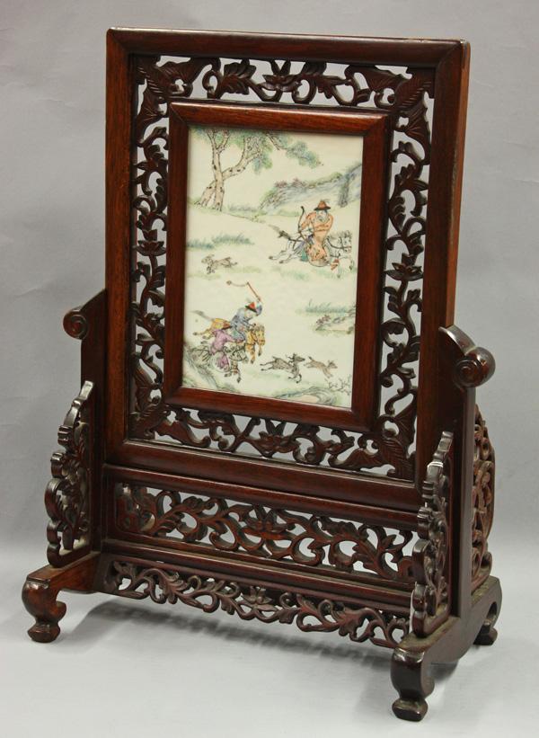 Chinese Painted Porcelain Table Screen: Chinese wooden table screen set an with enameled porcelain plaque, the panel depicting a dynamic scene of hunters on horseback chasing deers and other small animals, all set in an openwork wooden fram