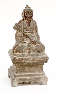 Chinese Stone Daoist Figure: Chinese stone figure of a Daoist immortal, seated on a straw mat resting on top of a high stepped plinth, the bearded divinity wearing the robes of a scholar-official and holding a fan to the front