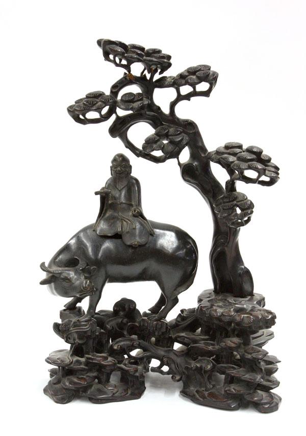 Chinese Metal/Wood Figural Group: Chinese patinated metal and wood figural group, featuring a sage with scroll in hand seated on a separately cast ox, all set on an elaborate ebonized wood stand carved and undercut with rockwork and l